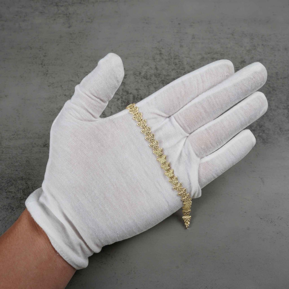 Open palm wearing a white glove holding a 10k gold butterfly bracelet.
