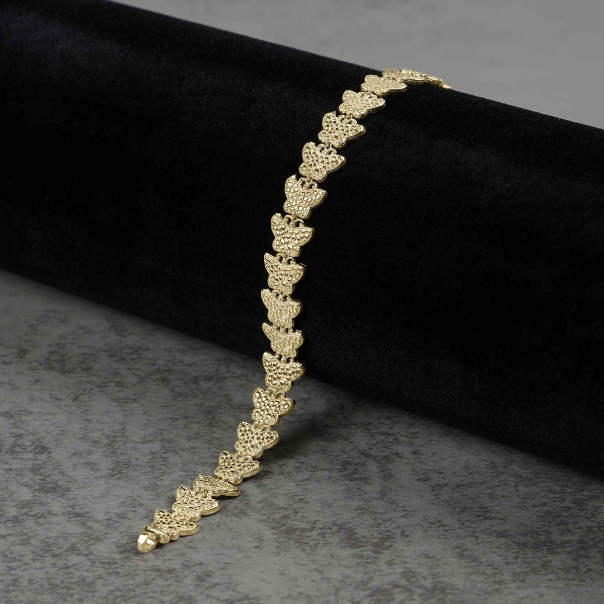 10k gold Forev nugget butterfly link bracelet draped on dark velvet and gray surface