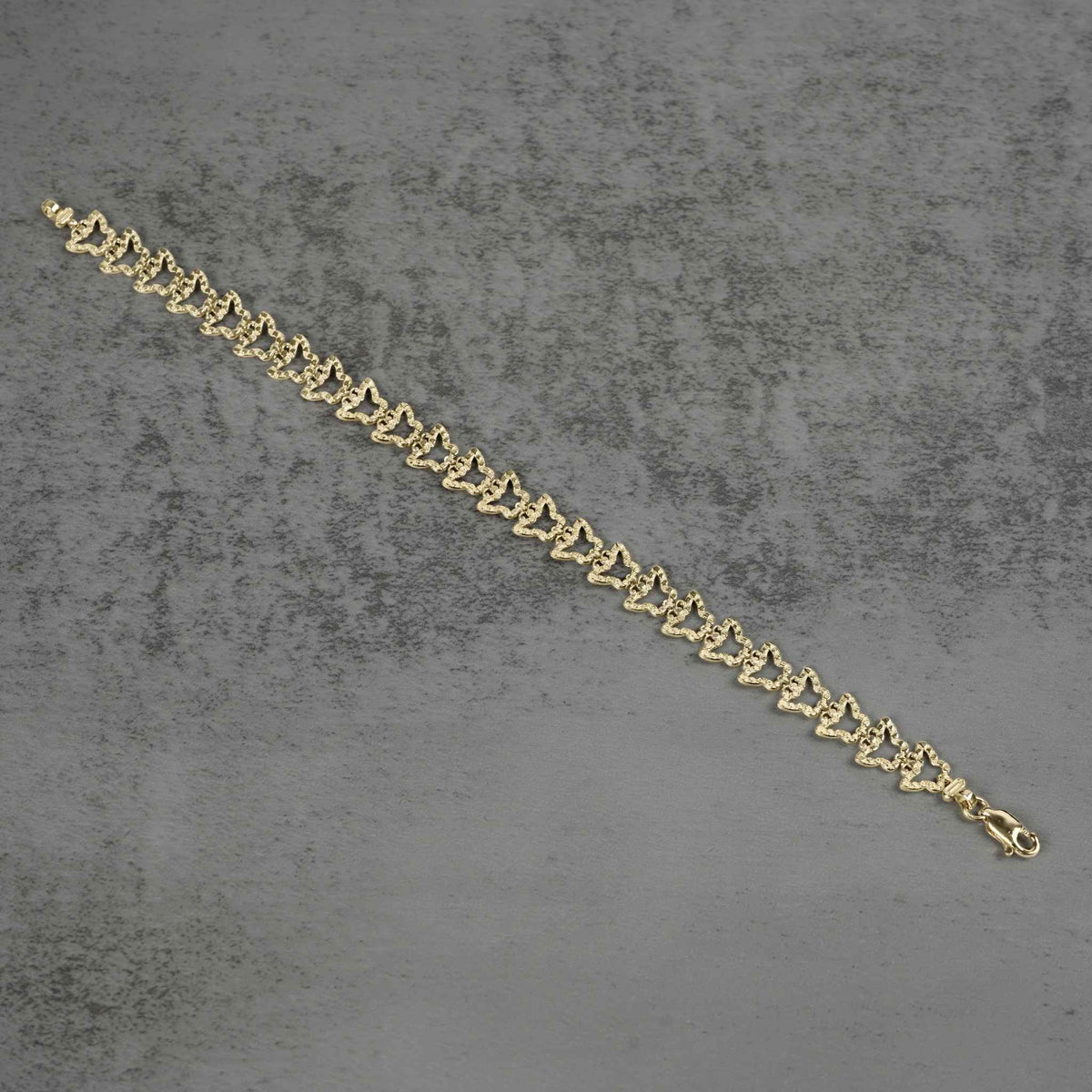10k gold nugget butterfly link bracelet laid flat diagonally on a gray surface.