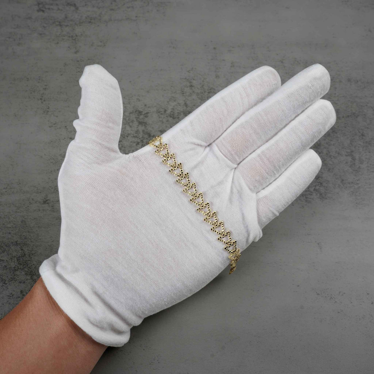 White gloved hand holding a 10k gold Amori nugget butterfly link bracelet.