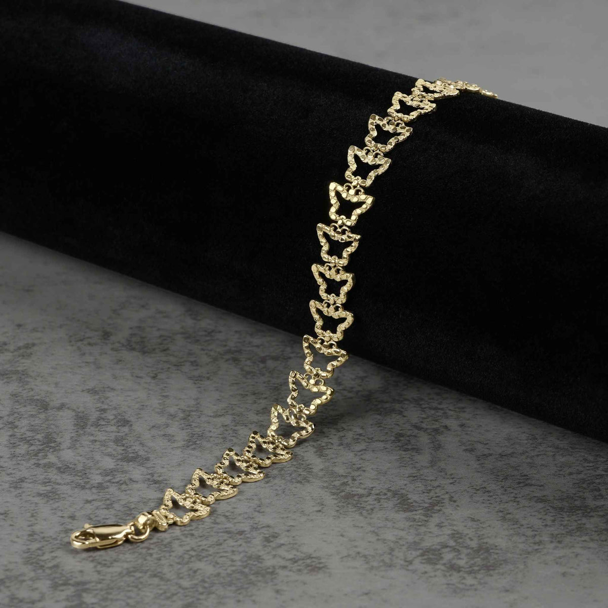 10k gold nugget butterfly link bracelet draped on dark velvet and gray surface.