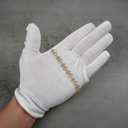 White-gloved hand holding a 10k yellow gold Amori nugget heart and cross link bracelet.