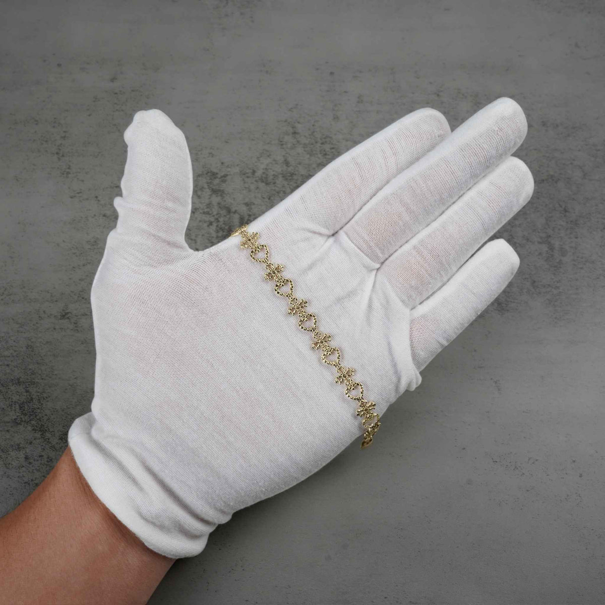 White-gloved hand holding a 10k yellow gold Amori nugget heart and cross link bracelet.