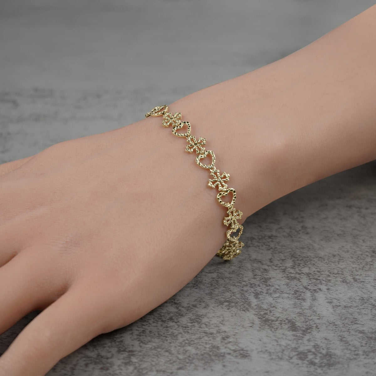 Model wearing a 10k yellow gold Amori nugget heart and cross link bracelet.