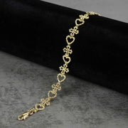 10k yellow gold Amori nugget heart and cross link bracelet on black display.