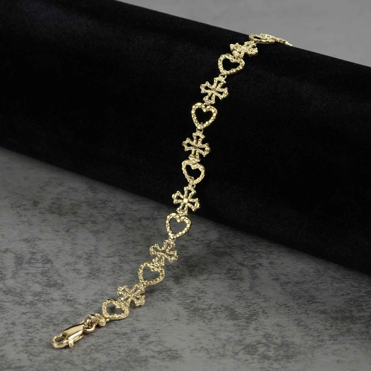 10k yellow gold Amori nugget heart and cross link bracelet on black display.