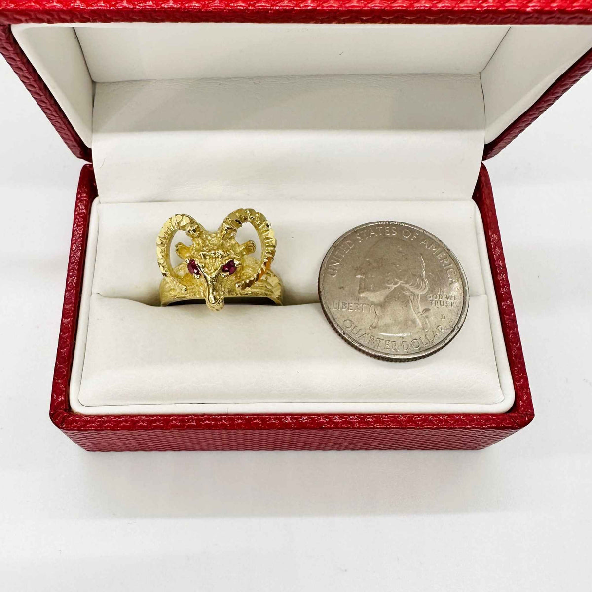 14k Gold ring with bighorn sheep red eye design next to a silver dollar coin