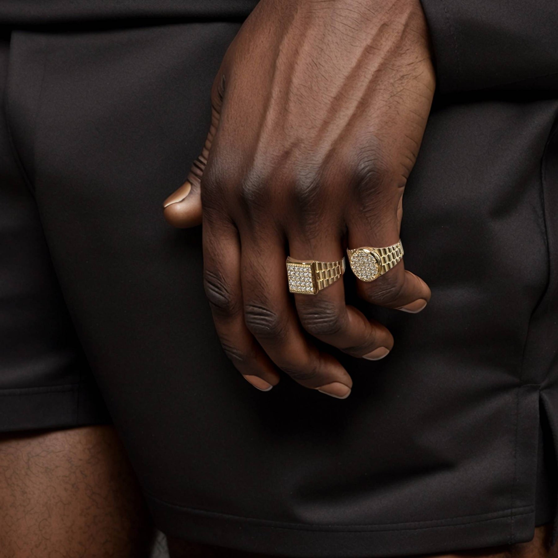 Two men's fine 10k gold cubic zirconia signet rings styled against dark clothing.