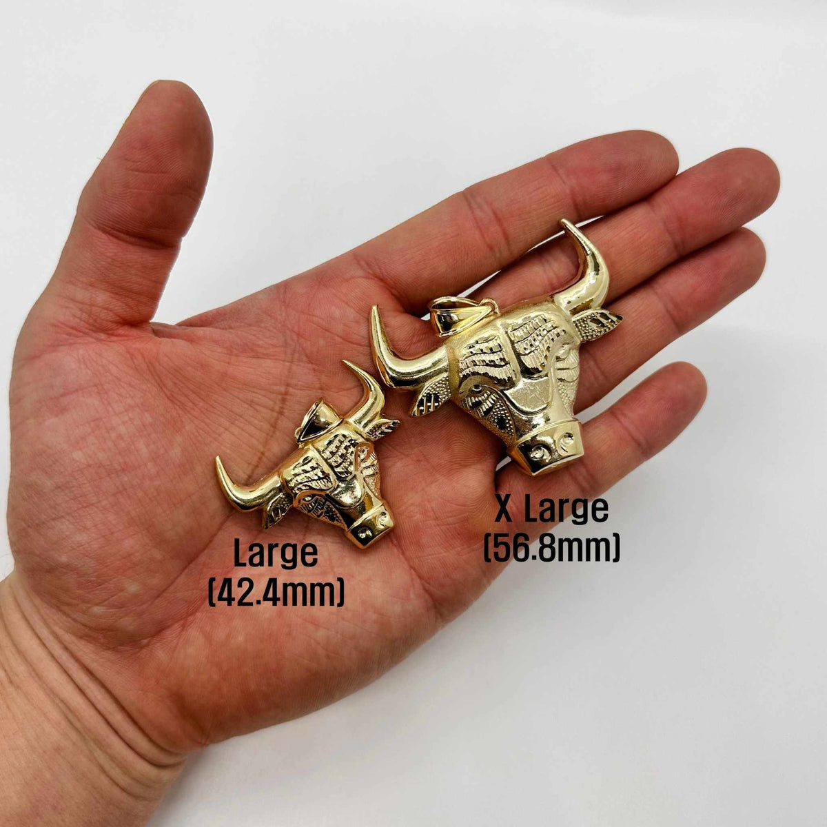 Hand holding two 10k gold Taurus bull head pendants with size label text.