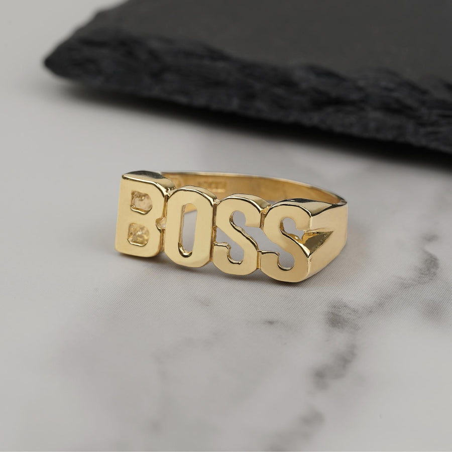 Polished 10k yellow gold BOSS statement ring resting on a marble surface