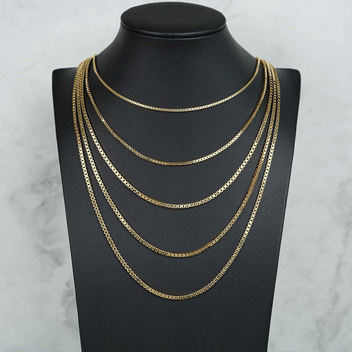 Four 10k yellow gold solid box chain necklaces layered on a black jewelry mannequin bust.