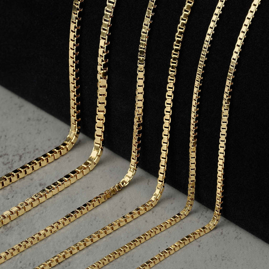 Six 10k yellow gold solid box chain necklaces arranged diagonally by increasing thickness on a black background.