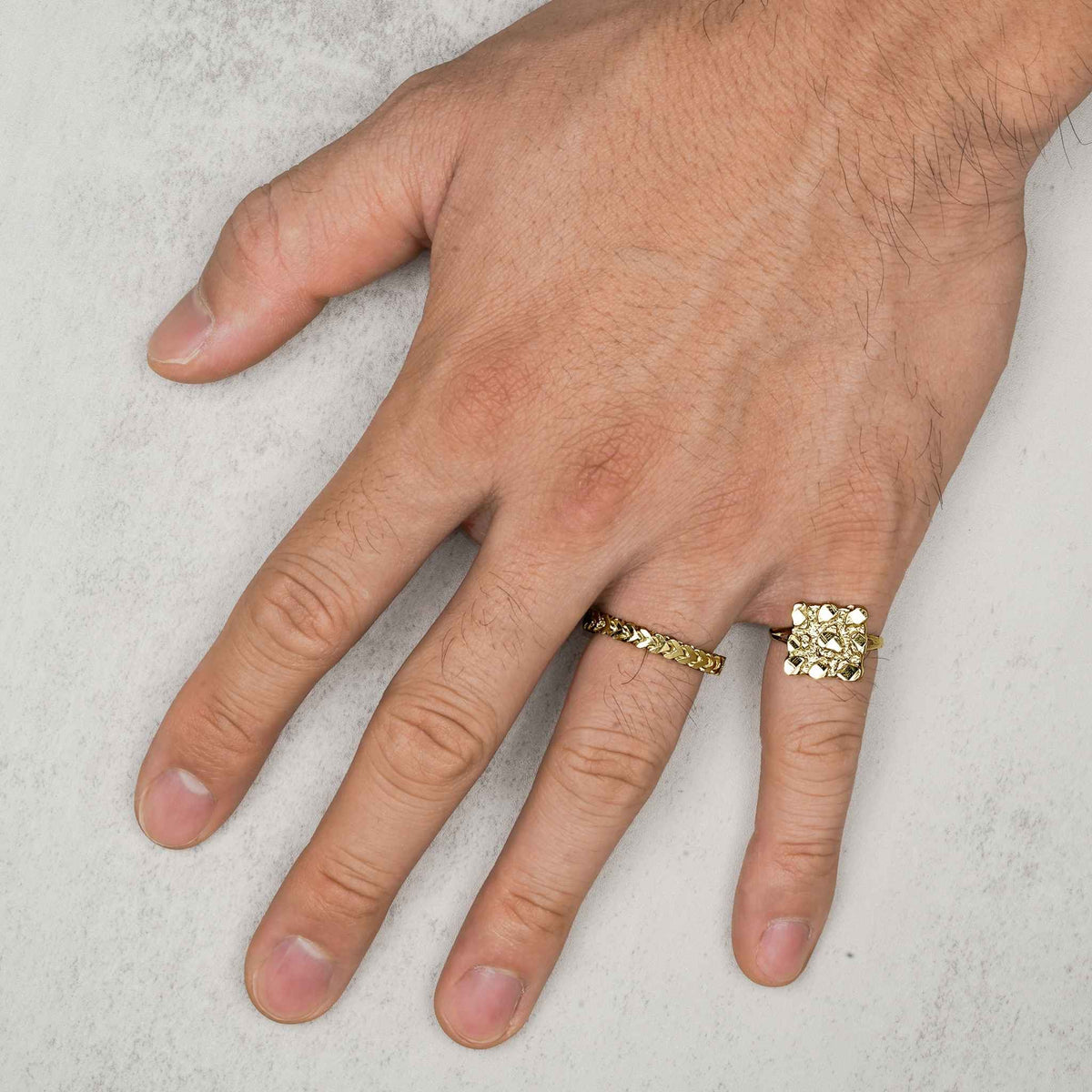 Model's hand wearing a 10k gold classic Franco band ring on a gray background.