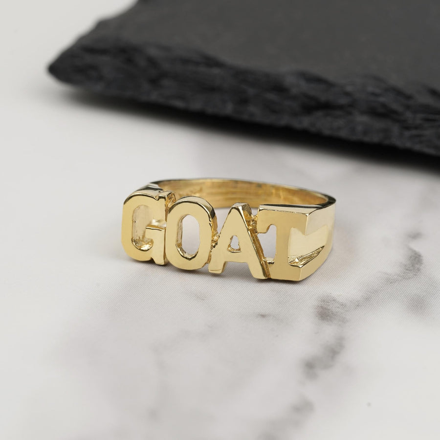 10k yellow gold ring with bold block letters spelling GOAT on marble surface.