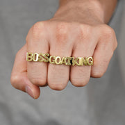 Model's fist wearing gold letter rings spelling BOSS GOAT KING.