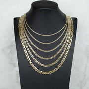 Seven 10k gold mariner chains of varying widths layered on a black jewelry bust.