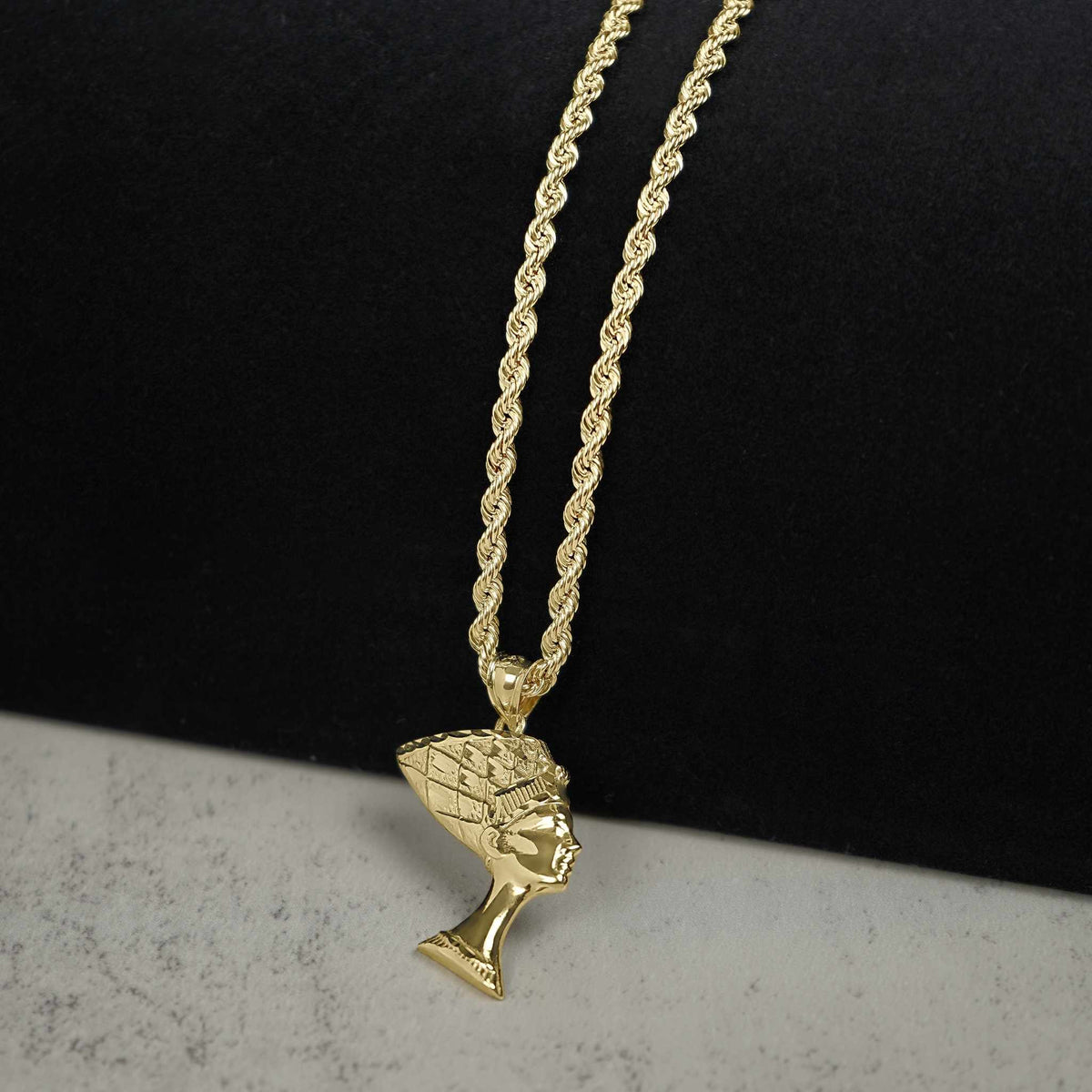Polished 10k gold Queen Nefertiti pendant on a rope chain against a split background.