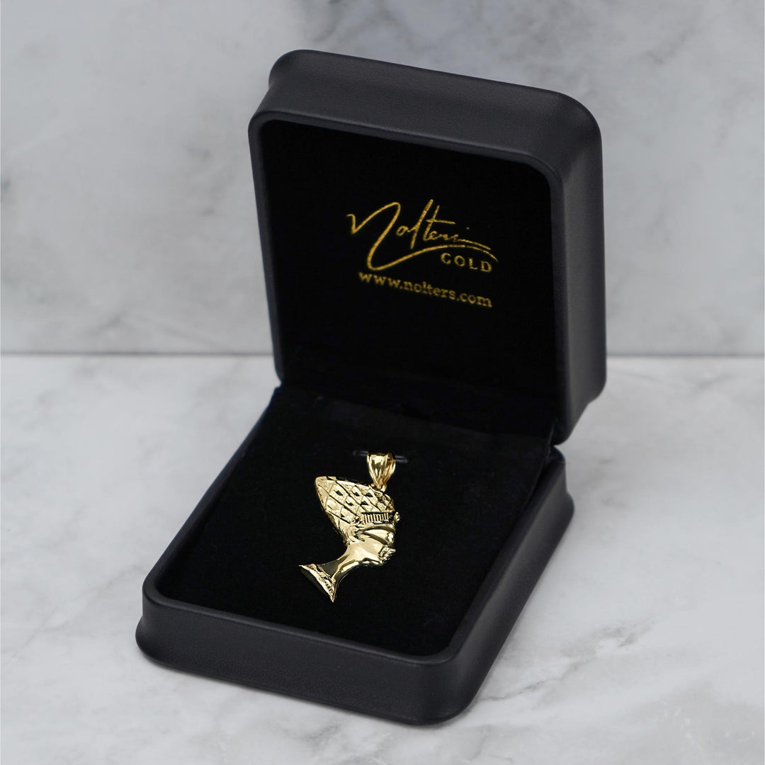 Gold Nefertiti pendant displayed in an open black jewelry box on a marble surface.