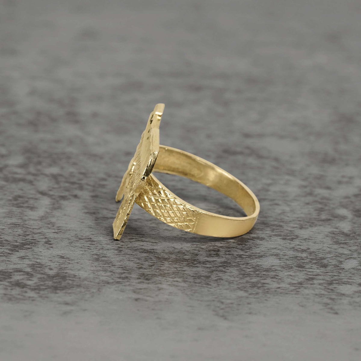Side view of 10k gold classic Uzi ring showcasing textured details on gray surface.