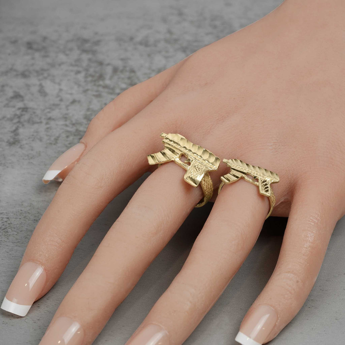 Mannequin hand with French tip nails wearing two 10k gold Uzi rings.