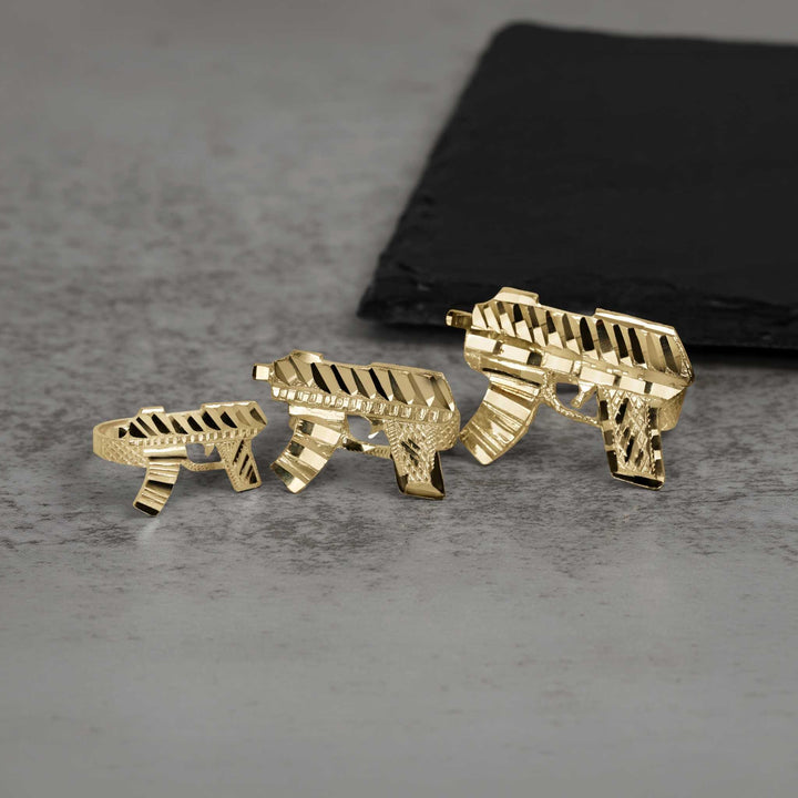 Three 10k gold classic Uzi gun rings displayed on a gray stone surface.