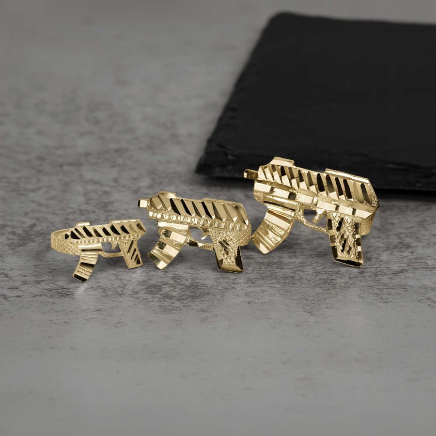 Three 10k gold classic Uzi gun rings displayed on a gray stone surface.