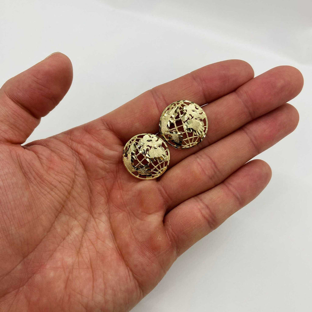 Pair of 10k gold globe stud earrings held in a hand for size reference.