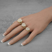 A hand displaying small, medium, and large yellow gold heart rings with cubic zirconia
