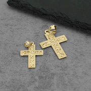 Back view of two textured gold cross pendants resting flat against a dark background.