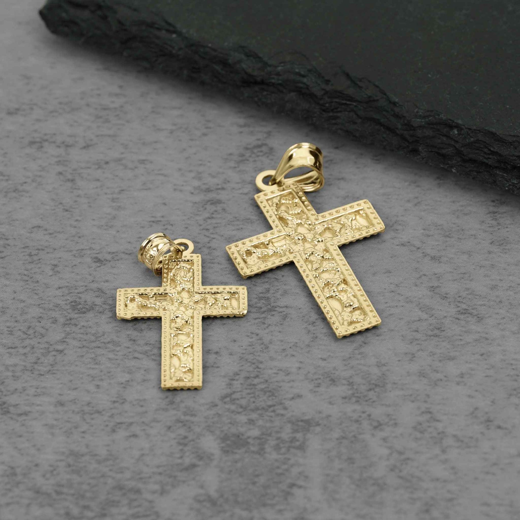 Back view of two textured gold cross pendants resting flat against a dark background.