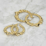 Assorted sizes of textured 10k gold interconnected heart hoop earrings on marble surface.
