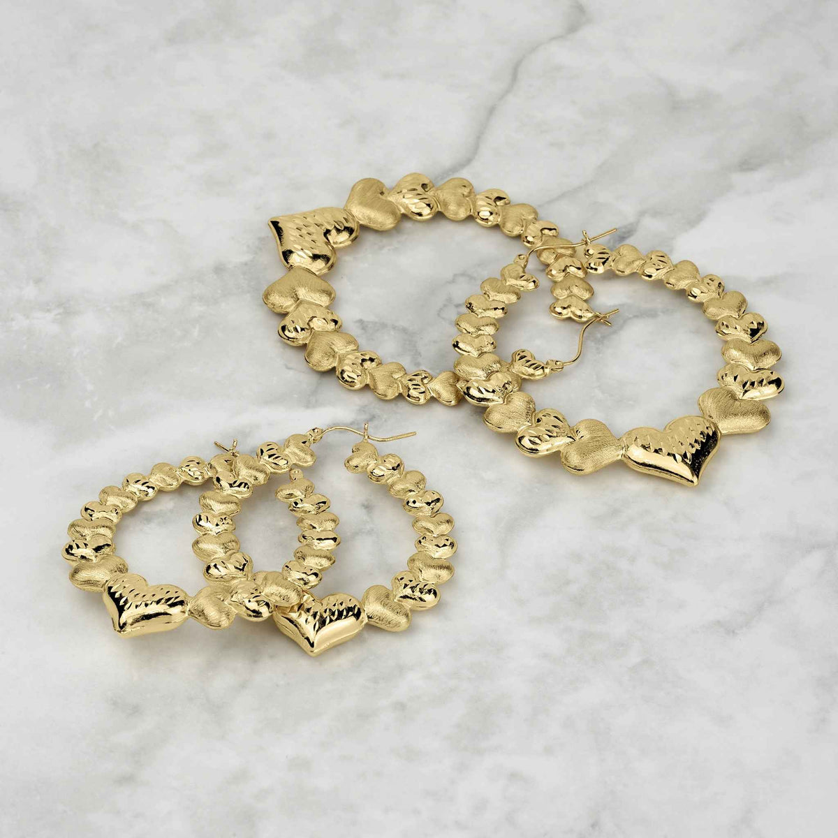 Assorted sizes of textured 10k gold interconnected heart hoop earrings on marble surface.