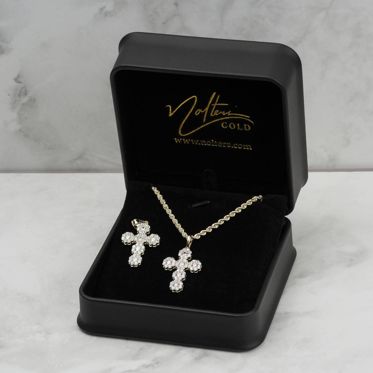 Two iced-out gold cross pendants featured inside an open black case against a light marble background.