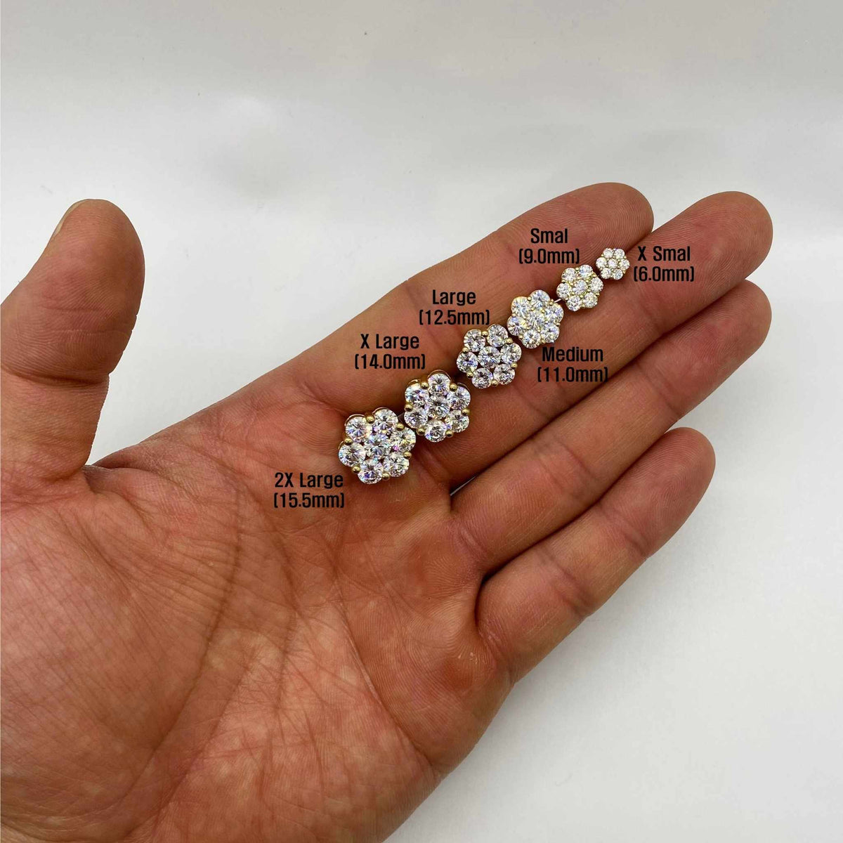 Hand holding six different sizes of gold hexagon flower cubic zirconia stud earrings.
