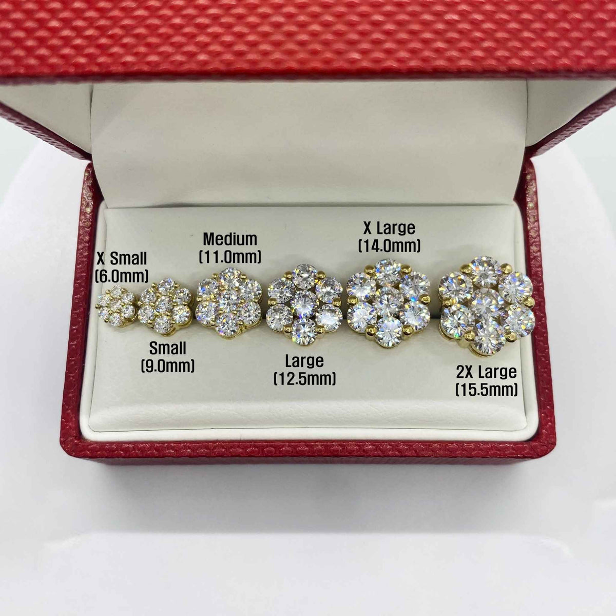 Six different sizes of gold hexagon flower cubic zirconia stud earrings arranged in a box.