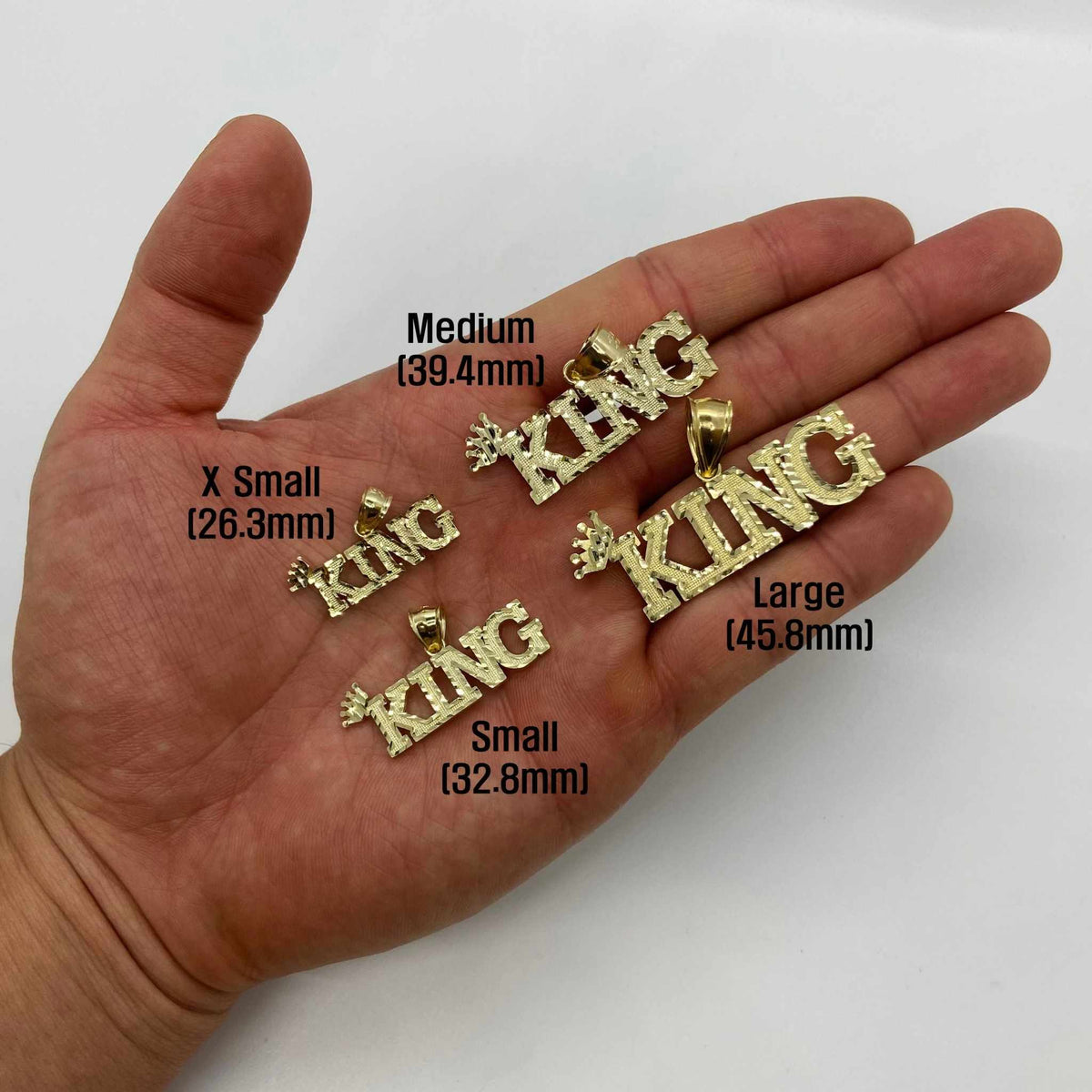 Four sizes of 10k gold King crown pendants displayed resting in an open hand.