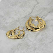Two sizes of 10k gold kissing dolphin hoop earrings on a light marble surface.