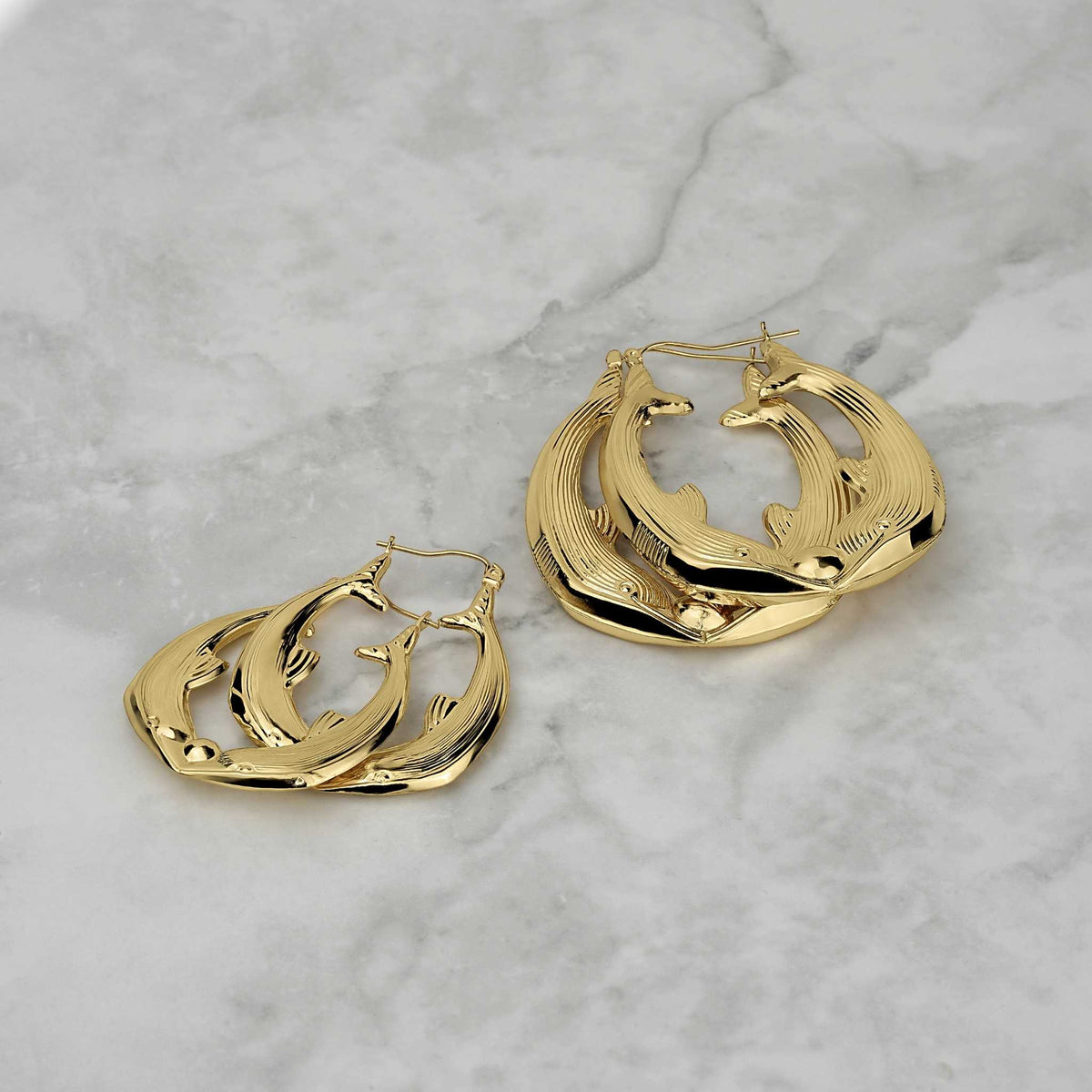 Two sizes of 10k gold kissing dolphin hoop earrings on a light marble surface.