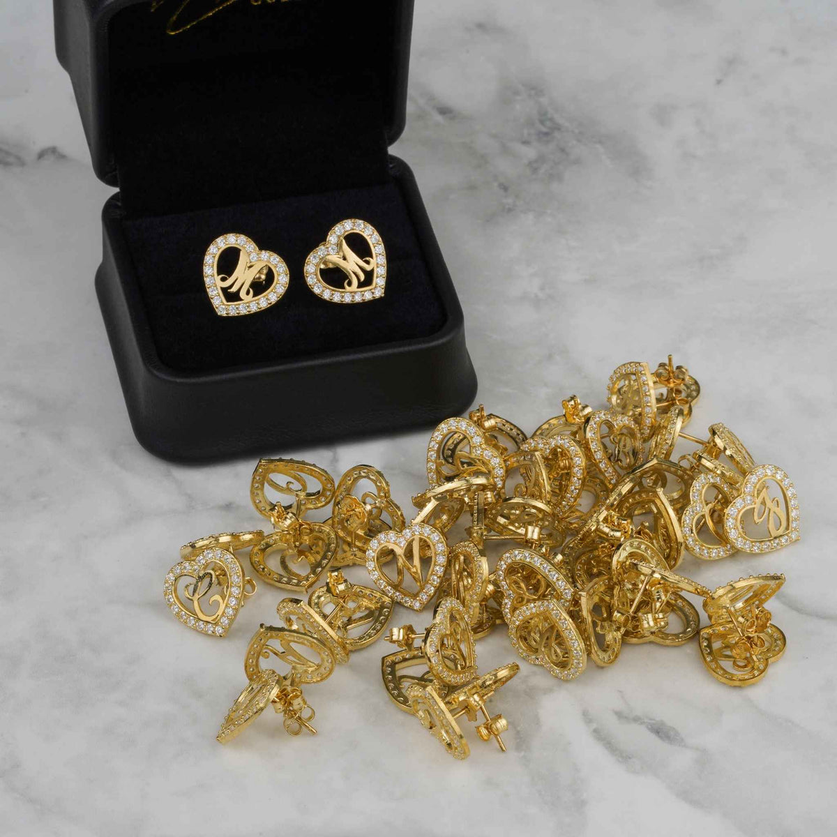 Assortment of 10k gold cursive initial heart stud earrings on a marble surface.