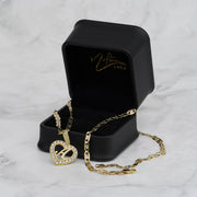 Gold heart pendant necklace and chain displayed in an open black gift box on marble.