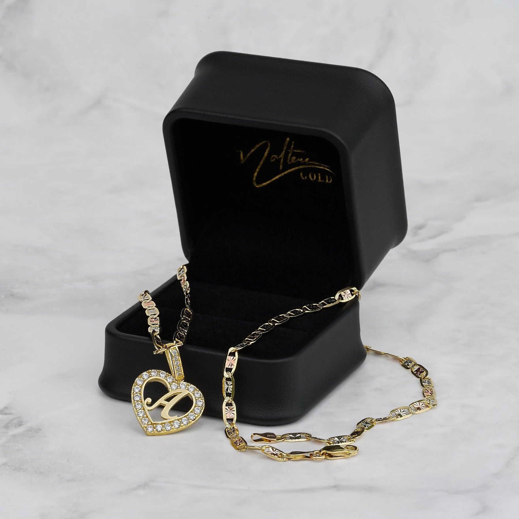 Gold heart pendant necklace and chain displayed in an open black gift box on marble.
