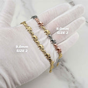 White-gloved hand displaying two 9.0mm Liora gold elephant link bracelets.