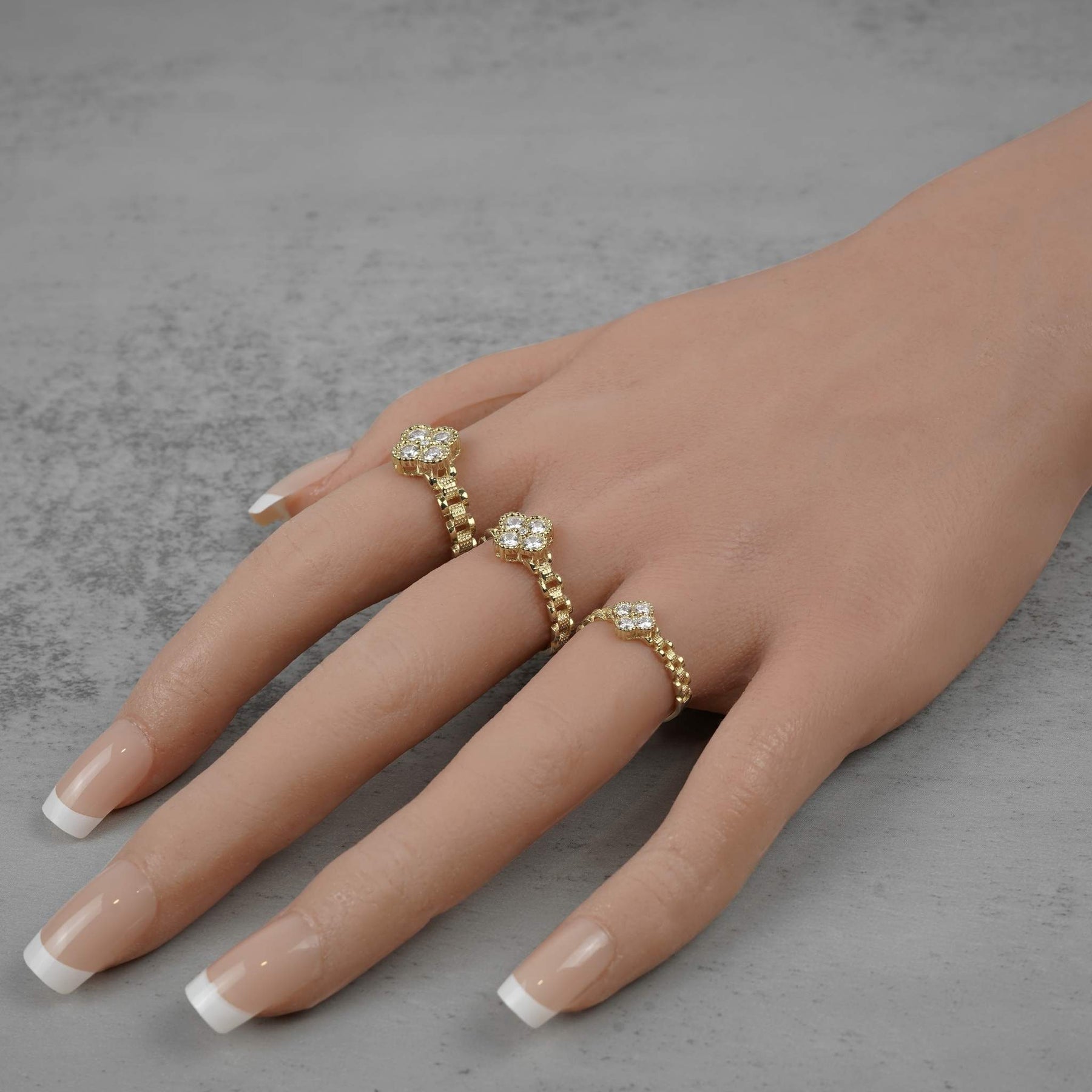 Three gold Rolex-style rings with white clover gemstone clusters worn on a hand.