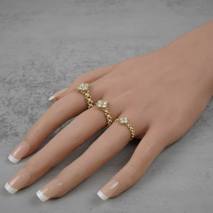 Three gold Rolex-style rings with white clover gemstone clusters worn on a hand.