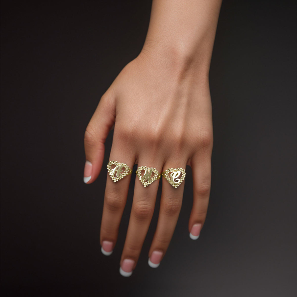 Model's hand wearing three 10k gold Luxe Rollie heart initial rings on fingers.