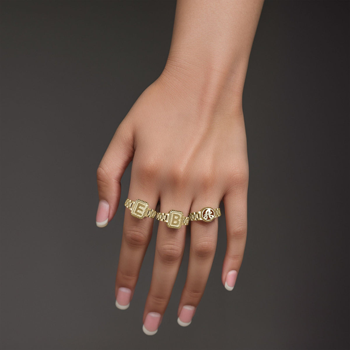 Model wearing three 10k gold luxe rectangular initial rings against a dark background.