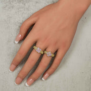 Two gold rings with pink gemstone clusters modeled on a person's fingers.