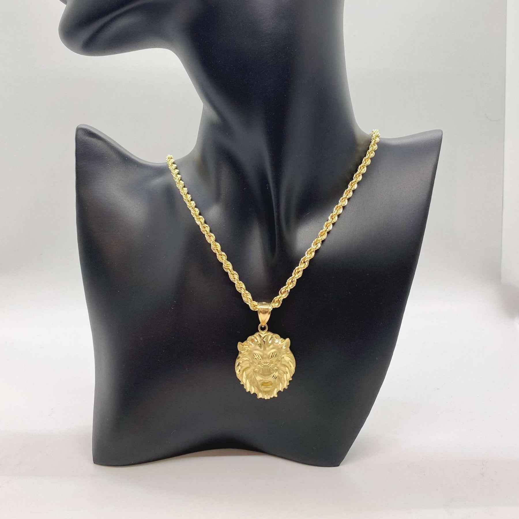 Gold lion head pendant on a rope chain displayed on a black jewelry bust