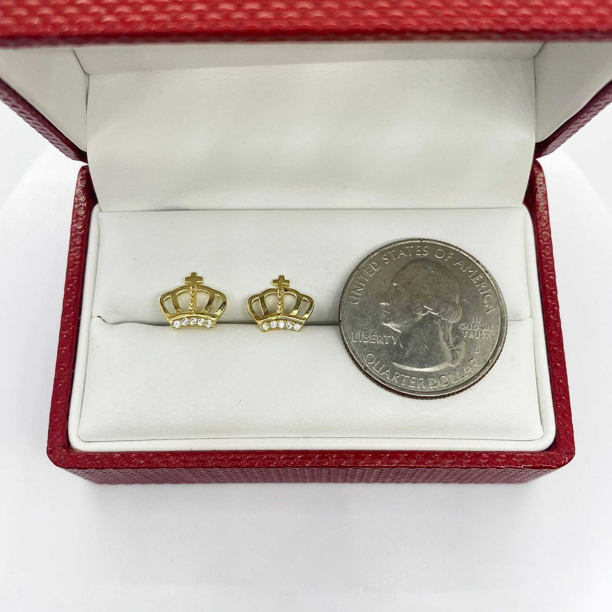 Gold crown-shaped earrings and a silver quarter dollar coin displayed in an open red jewelry box.