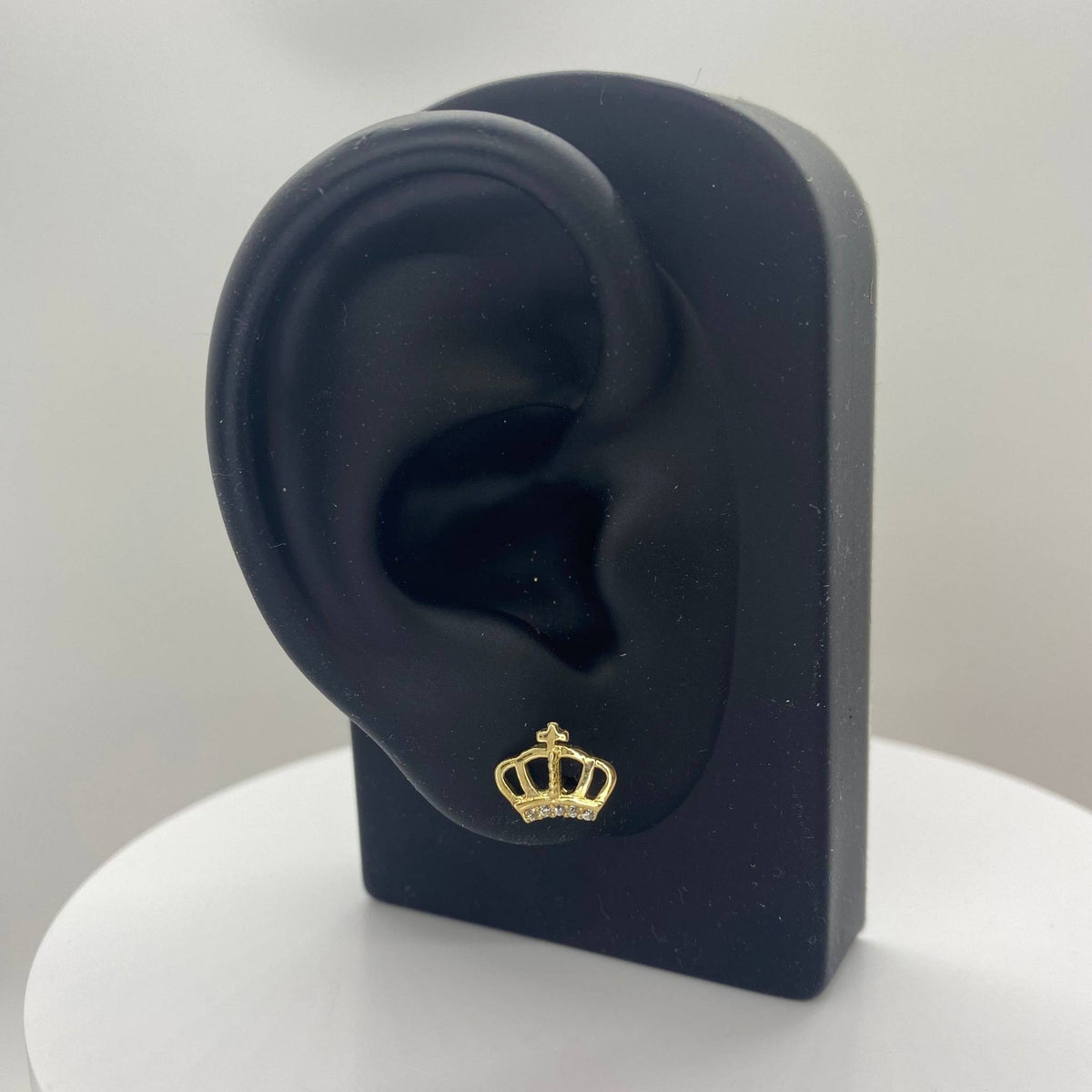Gold crown earring on a black ear model with a white background.